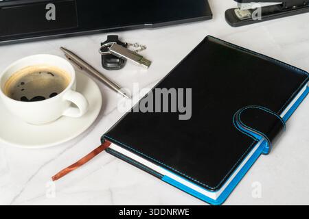Cahier noir, tasse à café, clés de voiture. Freelance Designer planification des tâches matinales à côté du bord de l'ordinateur portable, Journal en cuir et stylo, disposition minimaliste du bureau, S Banque D'Images