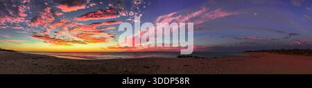 Une vue panoramique met en valeur un magnifique coucher de soleil sur l'océan, avec des couleurs vibrantes reflétant sur la mer calme et la plage de sable. Banque D'Images