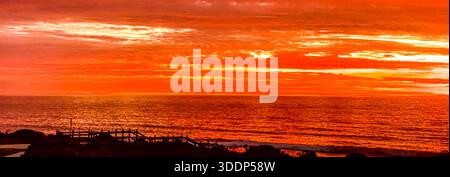 Un coucher de soleil spectaculaire présente des teintes orange et rouge vibrantes dans le ciel, illuminant les nuages sur l'océan serein. Banque D'Images
