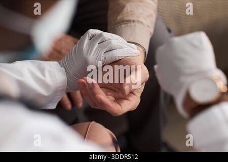Homme âgé caucasien recevant une assistance médicale d'un travailleur de la santé noir portant des gants, gros plan des mains montrant le soutien et les soins pendant l'examen de santé ou la consultation Banque D'Images