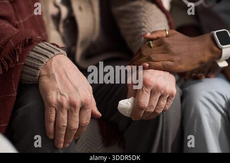 Homme caucasien senior assis avec les mains reposant sur les genoux, tenant le tissu, réconforté par une jeune femme noire posant doucement la main sur la sienne, montrant soutien et empathie Banque D'Images