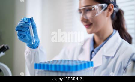 Chercheuse asiatique adulte examinant un liquide dans un tube à essai avec des gants dans un laboratoire. Focused Scientist mène d'importants travaux scientifiques en développant de nouveaux Banque D'Images