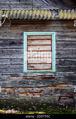 Fenêtre arborée de maison en bois abandonnée avec de la mousse poussant sur le mur Banque D'Images