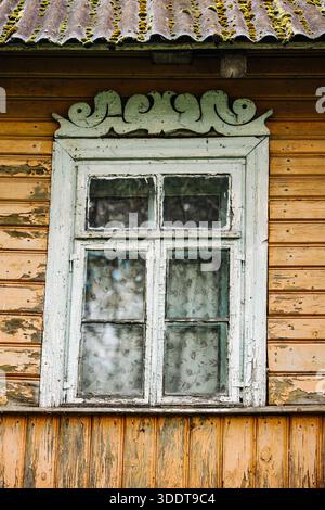 Vieille fenêtre altérée avec plateau sculpté et toit en mousse sur une maison en bois abandonnée Banque D'Images