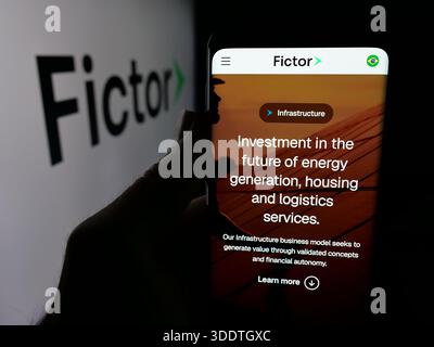 Dans cette illustration photo, une personne tient un smartphone avec la page Web de la société de conglomérat brésilien Grupo Fictor sur l'écran devant le logo. Banque D'Images