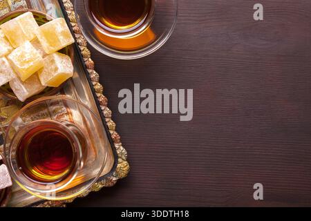 Un plateau avec délice turc et thé dans des tasses en verre traditionnelles sur un fond en bois brun foncé. Pose à plat. Banque D'Images