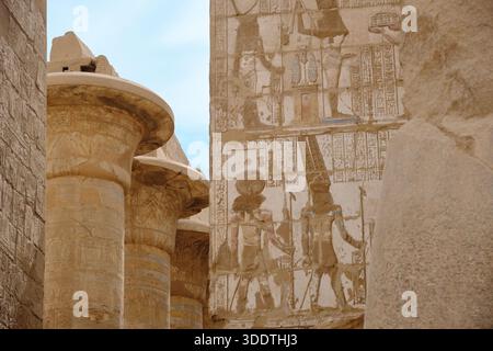 Anciens reliefs en pierre égyptiens sculptés dans les murs du temple, représentant des personnages humains et des scènes symboliques à côté de colonnes massives de grès. CA hiéroglyphique Banque D'Images