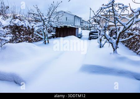 Belle vue sur le parking de la villa privée avec allée couverte de neige profonde, voitures et arbres de jardin en hiver. Suède. Banque D'Images