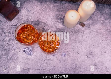 Vue aérienne de deux boissons de whisky avec de la glace sur la texture de béton fissuré, des bougies dans un coin et beaucoup d'espace de copie. Pose à plat minimale de la barre. Banque D'Images