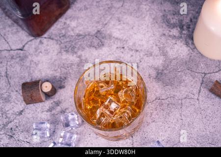Vue de dessus d'un verre à whisky avec des glaçons sur une surface en pierre, avec coin bouteille et bougie. Natures mortes à plat avec espace de copie pour les menus, la vie nocturne, Banque D'Images