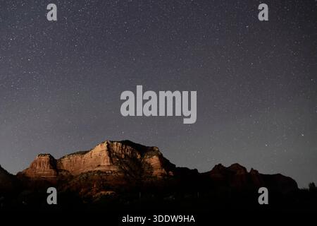 Étoiles denses à travers le ciel nocturne au-dessus des formations de grès à Bell Rock à Sedona, Arizona, États-Unis, avec de basses collines désertiques dans l'ombre en dessous. Banque D'Images
