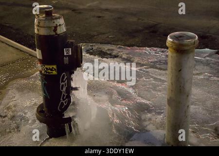 Les bornes d'incendie urbaines sont entourées d'un bassin de glace gelé sous la lueur des lampadaires, soulignant l'emprise tranquille de l'hiver sur les infrastructures de la ville. Banque D'Images