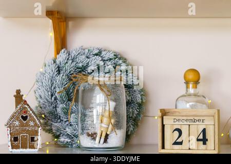 Style d'étagère de Noël festif avec maison en pain d'épices, calendrier de décembre en bois, décor de pot en verre et couronne enneigée. Intérieur confortable de vacances d'hiver avec Banque D'Images