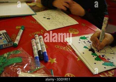 Plan en grand angle d'enfants coloriant des dessins festifs sur une nappe rouge de Noël avec des marqueurs et des ballons. Ambiance chaleureuse et authentique des activités de vacances Banque D'Images