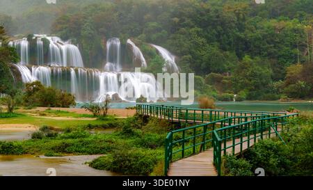 Cascades de Ban Gioc dans de larges couloirs en gradins dans une rivière turquoise, avec une passerelle piétonne courbe. Banque D'Images