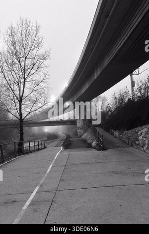 Une scène matinale brumeuse montre un chemin menant sous un pont. Le chemin se divise, offrant le choix de monter les escaliers ou de continuer le long de la rivière. Le brouillard obs Banque D'Images