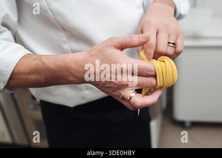 Un savoir-faire exquis façonne des Tagliatelles fraîches en nids uniformes en utilisant des méthodes manuelles méticuleuses Banque D'Images
