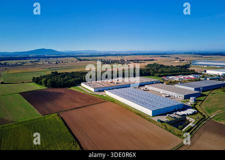 Vue aérienne du grand complexe d'entrepôt industriel et centre logistique dans la zone rurale avec des champs et des montagnes en arrière-plan Banque D'Images