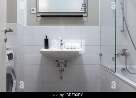Plan horizontal grand angle horizontal à hauteur des yeux d'une salle de bains carrelée de blanc propre avec un lavabo, une machine à laver et une douche vitrée dans un studio moderne Banque D'Images