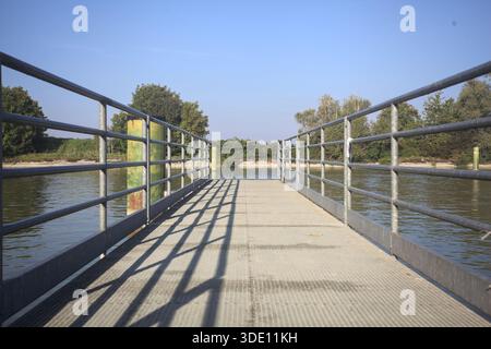 Jetée avec une promenade métallique sur un canal de diversion à côté des poteaux d'amarrage et la rive opposée avec des arbres Banque D'Images