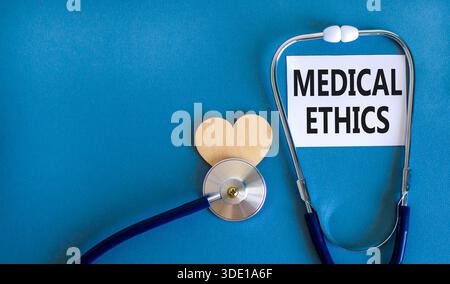 Symbole d'éthique médicale. Mots conceptuels éthique médicale sur une belle carte blanche. Coeur en bois et stéthoscope. Beau fond bleu. Médical sain Banque D'Images