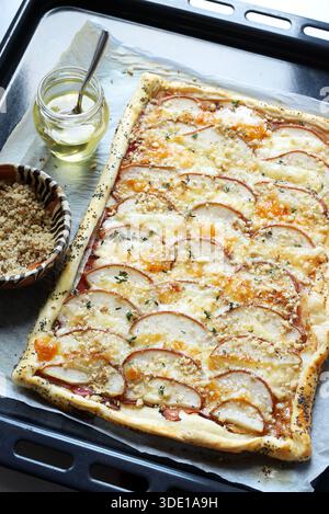 Tarte feuilletée salée au fromage et ​​pear finement tranchée, saupoudrée de noix hachées et garnie de thym frais et de miel. Vue de dessus. Banque D'Images