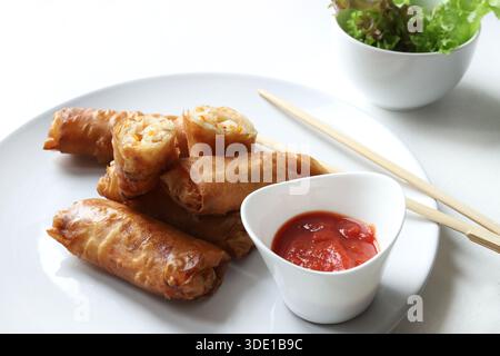 Rouleaux de printemps frits croustillants (rouleaux chinois) servis avec des baguettes, de la sauce rouge et de la laitue fraîche sur fond blanc. Plat typique de la cuisine asiatique. Banque D'Images