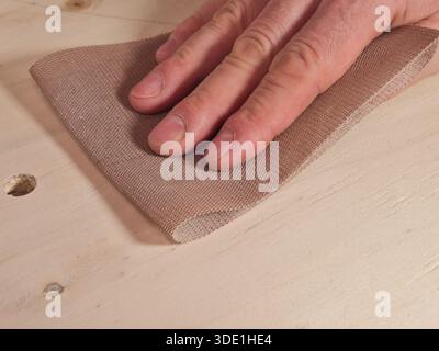 Ponçage à la main du bois avec maille abrasive gros plan ; gros plan de la main d'un charpentier ou d'un amateur de bricolage à l'aide de papier abrasif à maille moderne pour lisser et pré Banque D'Images