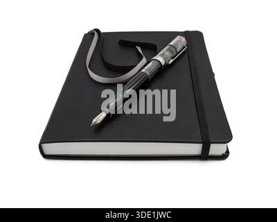 Un journal fermé à bande élastique noire et un stylo plume transparent positionné sur un fond blanc pour un look professionnel. Banque D'Images