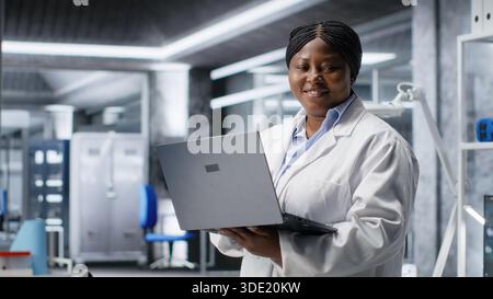 Afro-américaine scientifique travaille dans un laboratoire moderne, menant des expériences avec des équipements de pointe et un ordinateur portable. Biologie moléculaire, biotechnologie et innovation dans le domaine de la santé. Banque D'Images