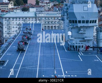Vue aérienne des hélicoptères alignés sur le pont du LHD Trieste, sa tour de contrôle de vol proéminente contre le paysage urbain, Trieste, Italie. Banque D'Images