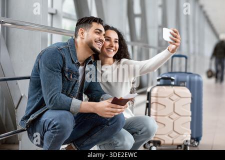Un jeune couple arabe heureux prend Selfie sur un smartphone à l'aéroport Banque D'Images