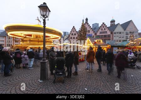 22 décembre 2025, marché de Noël de Francfort sur Roemerberg avec la ligne d'horizon en arrière-plan au crépuscule. Les lumières brillent et les enfants sont carous Banque D'Images