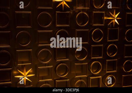 un mur texturé doré avec un motif répétitif de carrés et de cercles en relief. Un luminaire en forme d'étoile brille de manière éclatante, projetant une lumière chaude et Banque D'Images