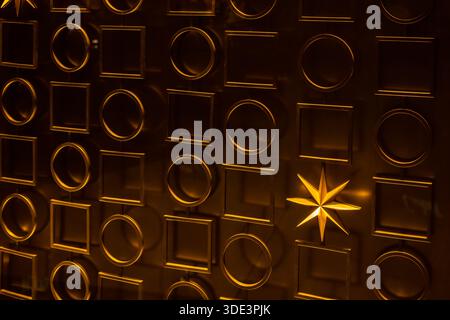 un mur texturé doré avec un motif répétitif de carrés et de cercles en relief. Un luminaire en forme d'étoile brille de manière éclatante, projetant une lumière chaude et Banque D'Images