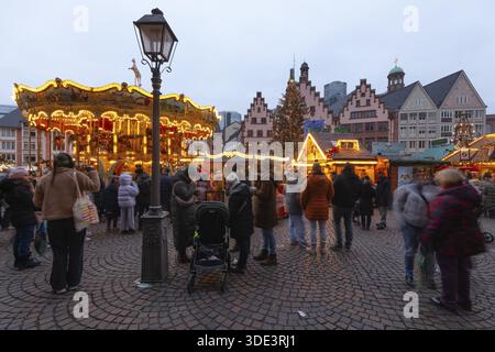 22 décembre 2025, marché de Noël de Francfort sur Roemerberg avec la ligne d'horizon en arrière-plan au crépuscule. Les lumières brillent et les enfants sont carous Banque D'Images