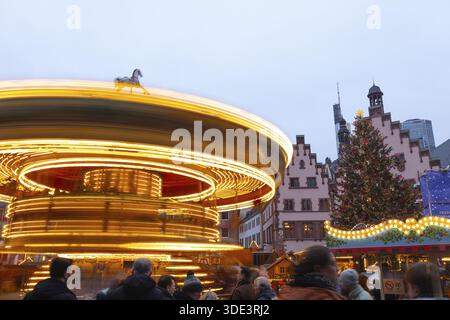 22 décembre 2025, marché de Noël de Francfort sur Roemerberg avec la ligne d'horizon en arrière-plan au crépuscule. Les lumières brillent et les enfants sont carous Banque D'Images