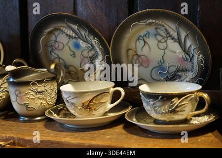 Kedah, Malaisie, 5 décembre 2025 : ensemble complexe de thé en porcelaine sur le thème du dragon avec théière, tasses et assiettes sur une étagère en bois rustique dans un cadre de café. Banque D'Images