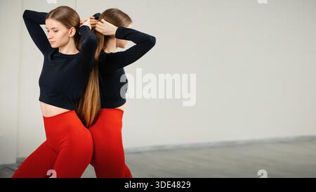 Jeune femme en top crop noir et leggings rouges attachant sa longue ha Banque D'Images