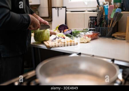 Gros plan sur le chef professionnel préparant des ingrédients pour un repas végétarien dans la cuisine du restaurant. Il coupe du chou. Banque D'Images