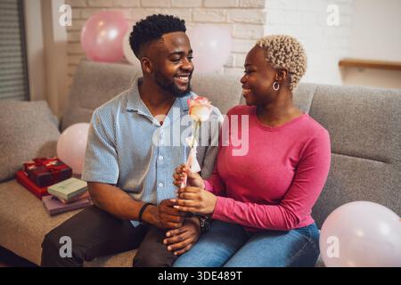 Heureux couple aimant célébrant l'anniversaire de la femme à la maison. Petit ami donne de la rose à sa petite amie. Banque D'Images