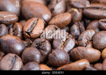 Gros plan sur les grains de café torréfiés capturés en macro, éclat d'huile brillant, tons bruns riches, fissures visibles des grains, surface texturée, eclairage de studio chaleureux, confortable Banque D'Images