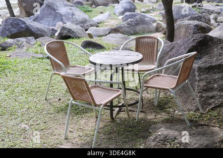 Mobilier d'extérieur avec chaises vides et table ronde assis paisiblement sur l'herbe verte dans le jardin entouré de grands rochers de pierre naturelle et tre Banque D'Images