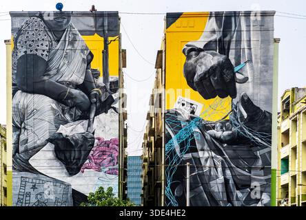 Grandes peintures murales en noir et blanc sur deux bâtiments adjacents représentant des mains et une femme en tenue traditionnelle, avec des accents colorés. Banque D'Images