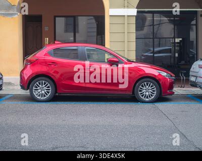 Une Mazda 2 à hayon rouge vif est garée à un endroit désigné sur une rue pavée, mettant en valeur son design moderne et sa taille compacte Banque D'Images