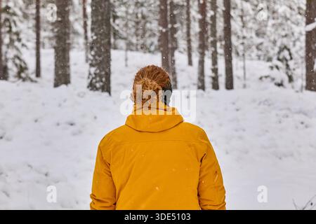Une femme dans une veste de couleur vive se tient dans une forêt enneigée Banque D'Images