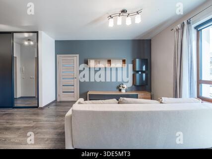 Salon lumineux avec des meubles modernes, un mur d'accent bleu et un décor propre, créant une atmosphère confortable et élégante. Banque D'Images