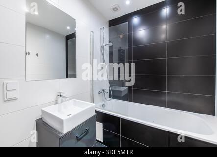 Une salle de bains contemporaine avec des murs carrelés noirs, une baignoire, un lavabo et des éléments de style minimaliste pour un aspect élégant et épuré Banque D'Images