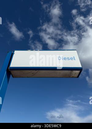 Vue minimaliste d'un panneau de station-service diesel vu d'en bas, posé contre un ciel bleu profond avec des nuages légers. L'image véhicule des thèmes d'énergie Banque D'Images