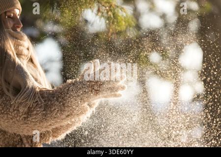 Gros plan des mains de femme dans des gants tricotés blancs, applaudissez et serrez les mains hors de la neige lors de la journée ensoleillée d'hiver Banque D'Images